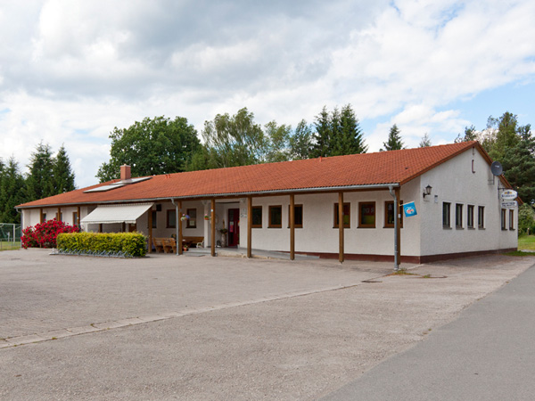 Flachbau des VfB-Sportheims mit überdachter Terrasse und Parkplatz am Waldrand
