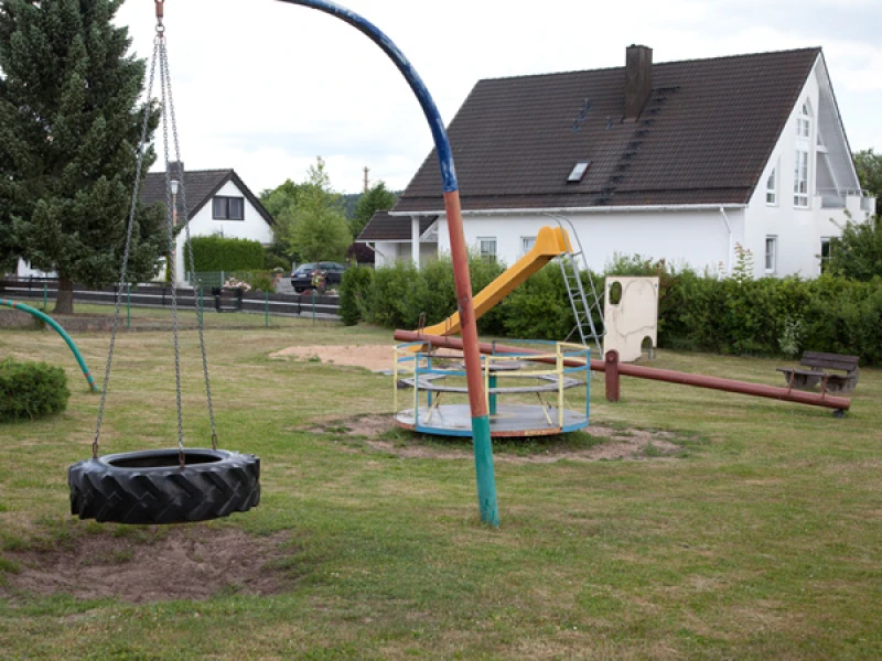Spielplatz mit Reifenschaukel, Karussell, Rutsche und Wippe in Wohnsiedlung
