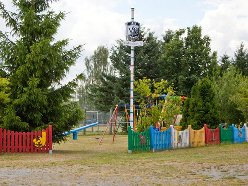 Bunt eingezäunter VfB-Kinderspielplatz mit Schaukel und Vereinsschild am Maibaum