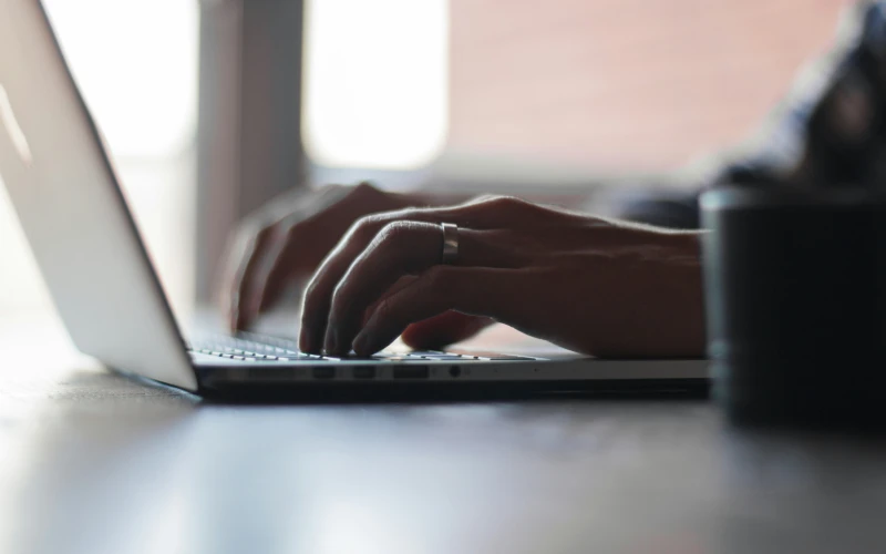 Hände schreiben auf Laptop, Laptop liegt auf einem Tische